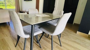 Un espace repas avec une table en verre et des chaises à revêtement gris, un plancher en bois et une vue sur la verdure à l’extérieur.