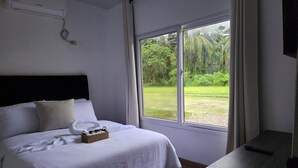 Une chambre à coucher comprenant un lit, une table de chevet, un téléviseur et une fenêtre donnant sur un paysage verdoyant.