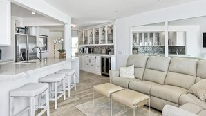 A modern kitchen with white cabinetry, a marble island, and bar stools.