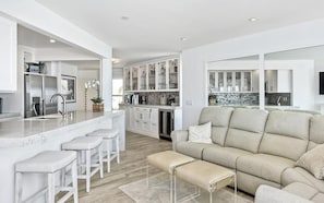 A modern kitchen with white cabinetry, a marble island, and bar stools.