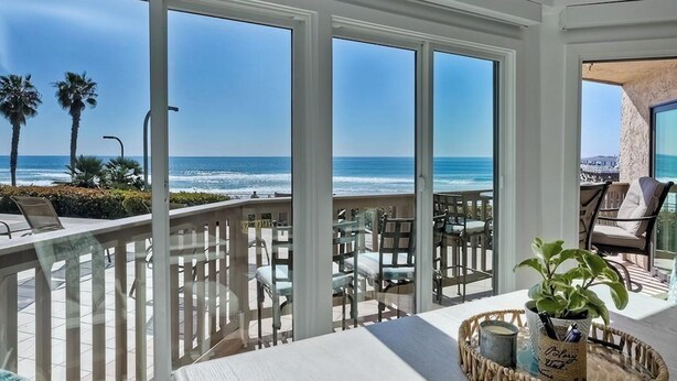 A balcony with a view of the ocean, outdoor furniture, and a potted plant.