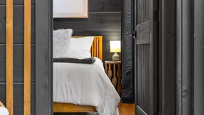 A bedroom with a bed, a nightstand, a lamp, and a door. - Romantic Cabin - Hot Tub, Fire Pit Near Gatlinburg (Sevierville)