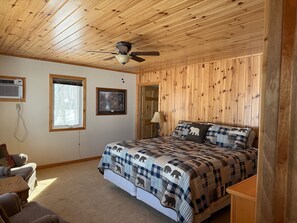 Ein Schlafzimmer mit Holzboden, einem Bett mit karierter Decke, einem Fenster und einer Tür.