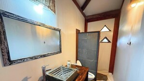 Un baño con tocador de madera, un espejo grande, inodoro y zona de ducha.