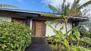 Un sendero conduce a un edificio con puerta de madera, rodeado de follaje y un cielo despejado.