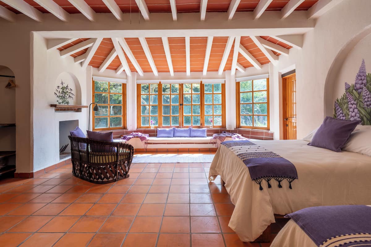 A spacious room with a high ceiling, large windows, a fireplace, and a bed with a purple blanket.
