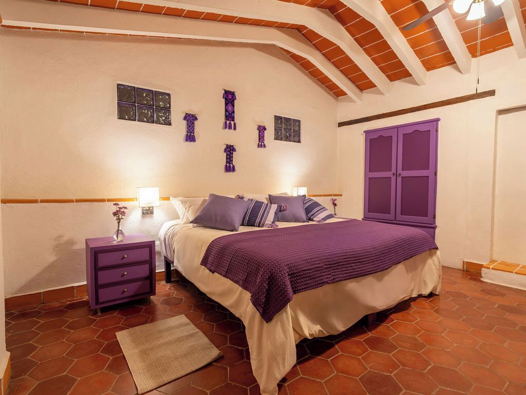 Un dormitorio con cama, mesitas de noche moradas, un armario morado y suelo de baldosas.