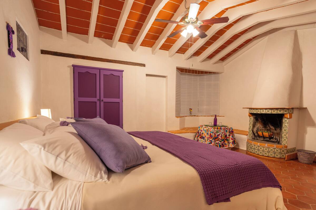 A bedroom with a bed, a purple wardrobe, a fireplace, and a ceiling fan.