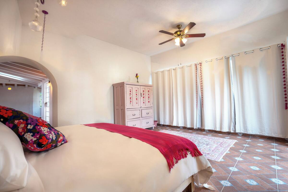 A bedroom with a bed, a ceiling fan, a dresser, and a window with curtains.