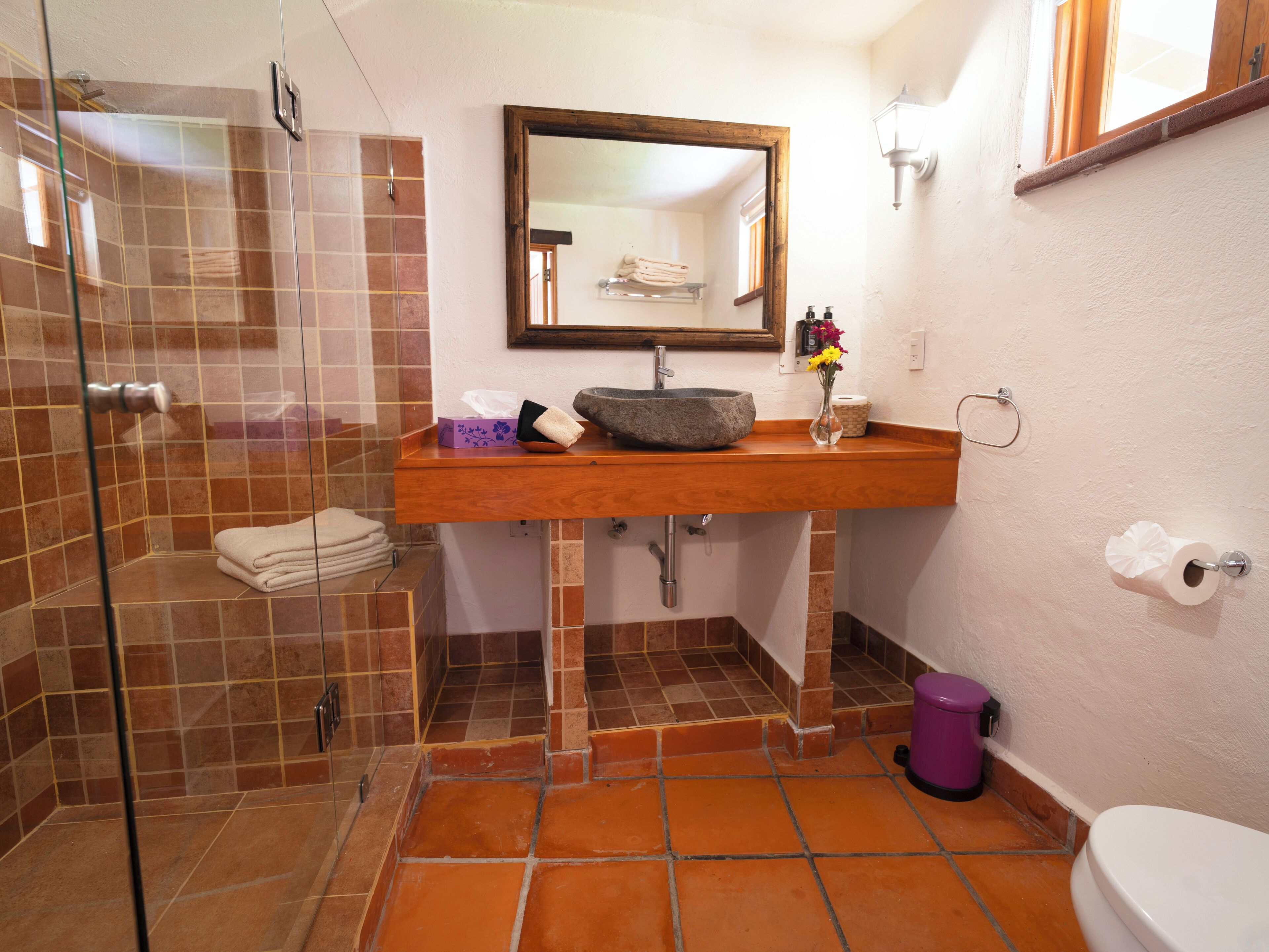 Un baño con cabina de ducha de vidrio, tocador de madera con lavabo de piedra, espejo sobre el lavabo y un inodoro.