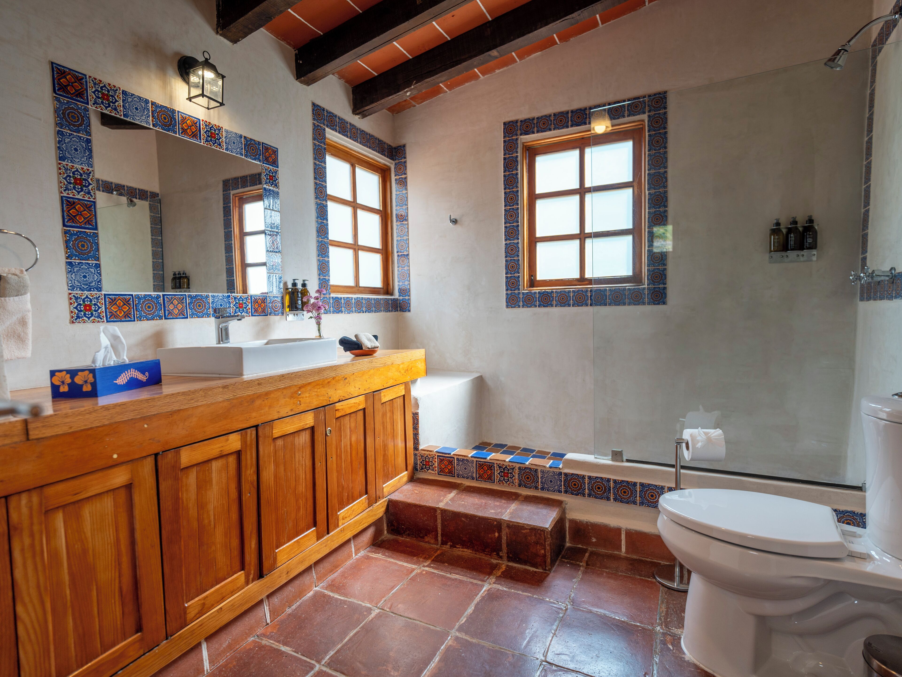 A bathroom with a wooden vanity, a large mirror, two windows, a bathtub, and a toilet.