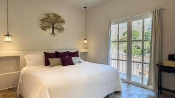 Une chambre avec un grand lit, un ventilateur de plafond, une décoration murale représentant un arbre et une vue à travers une porte vitrée.