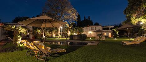 A backyard with a swimming pool, lounge chairs, and umbrellas.