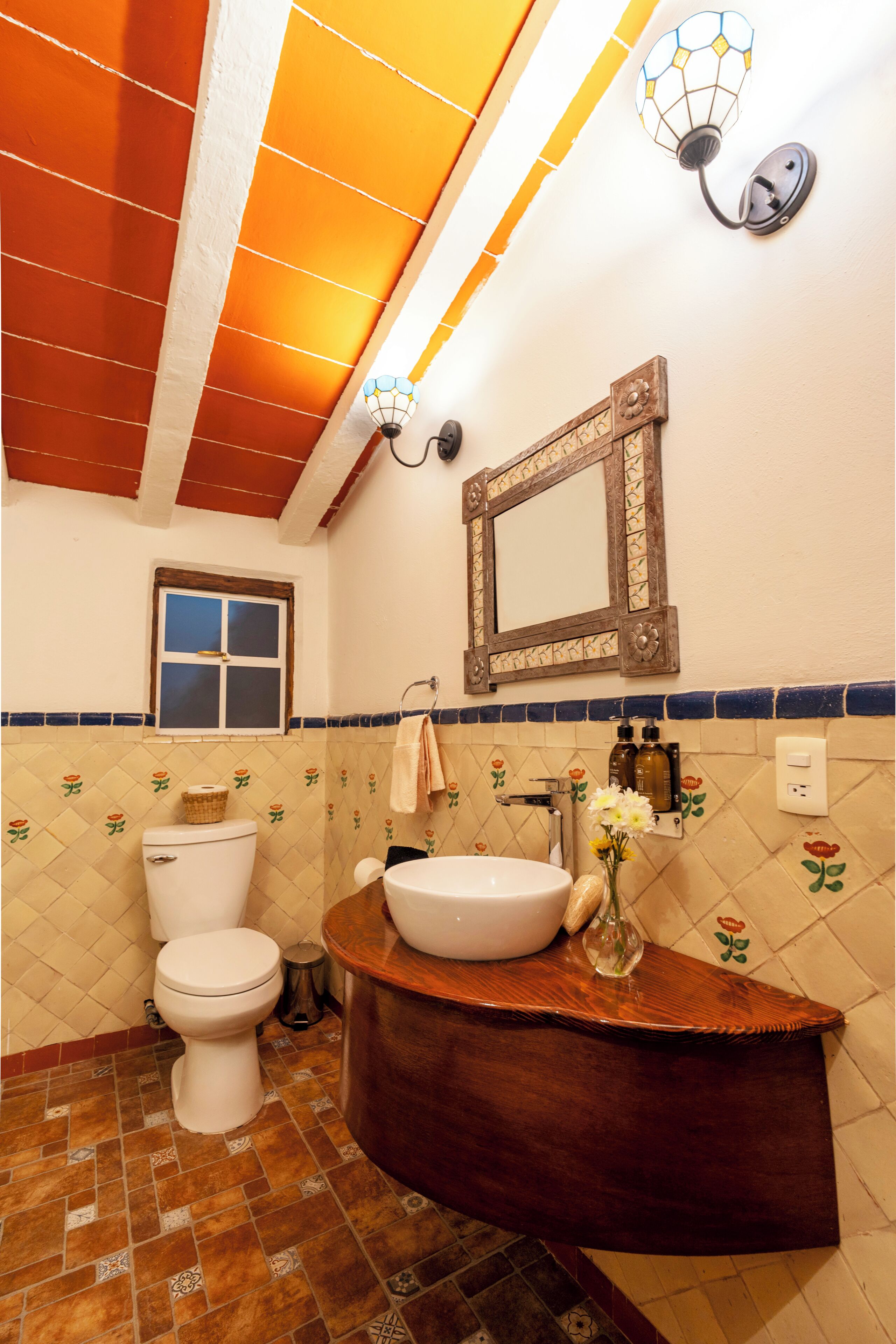A bathroom with a toilet, sink, mirror, and decorative tiles.