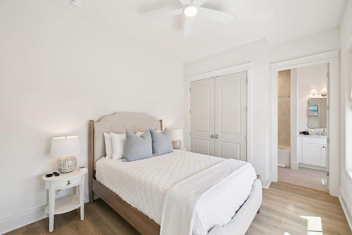Una camera da letto con un letto, comodini, una ventola a soffitto e una porta che dà su un bagno.