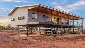 Una casa de dos pisos con un balcón techado, un garaje cubierto y un depósito de agua grande.
