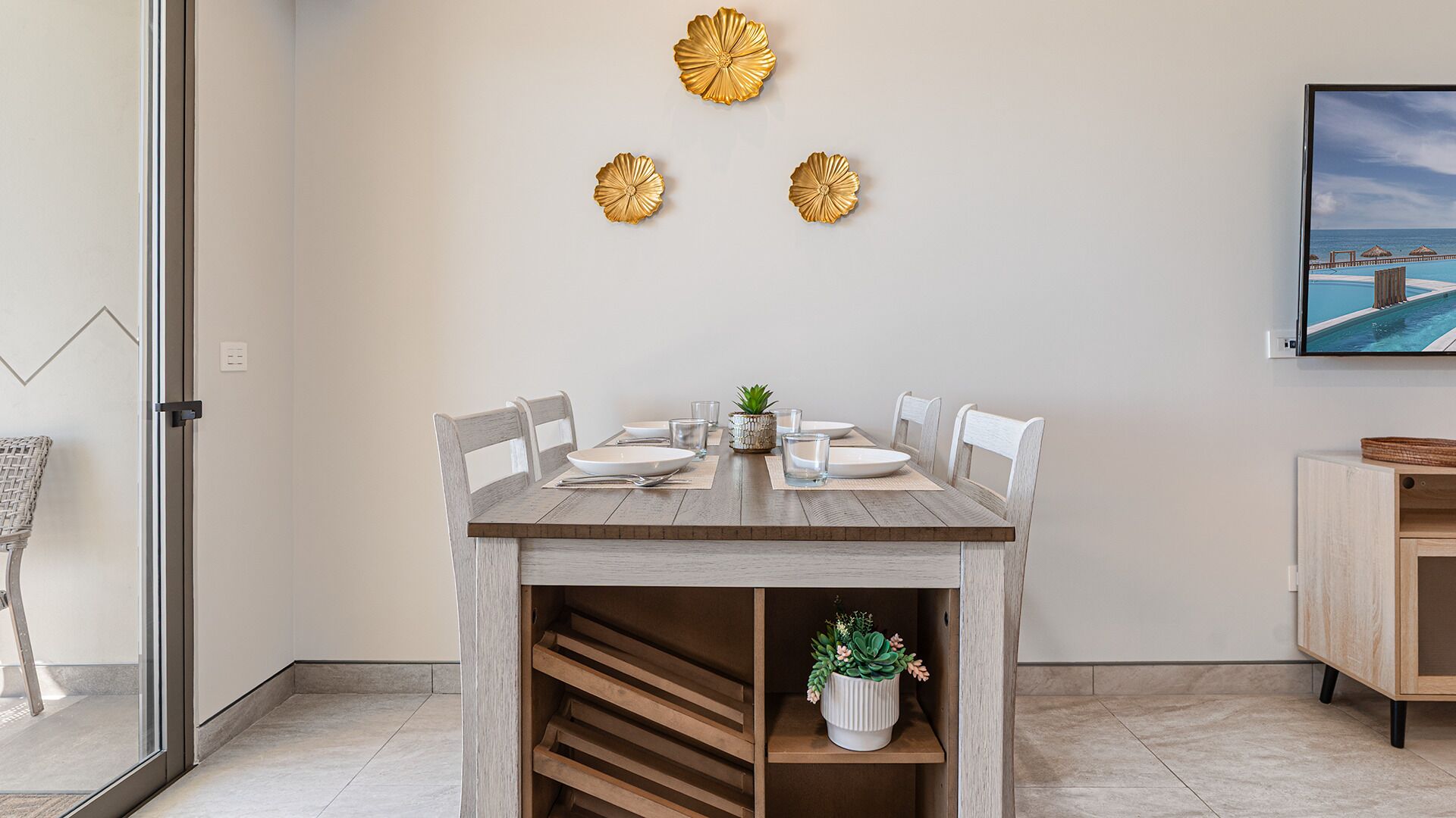 Un coin repas avec une table en bois, des chaises blanches et une petite plante en pot.