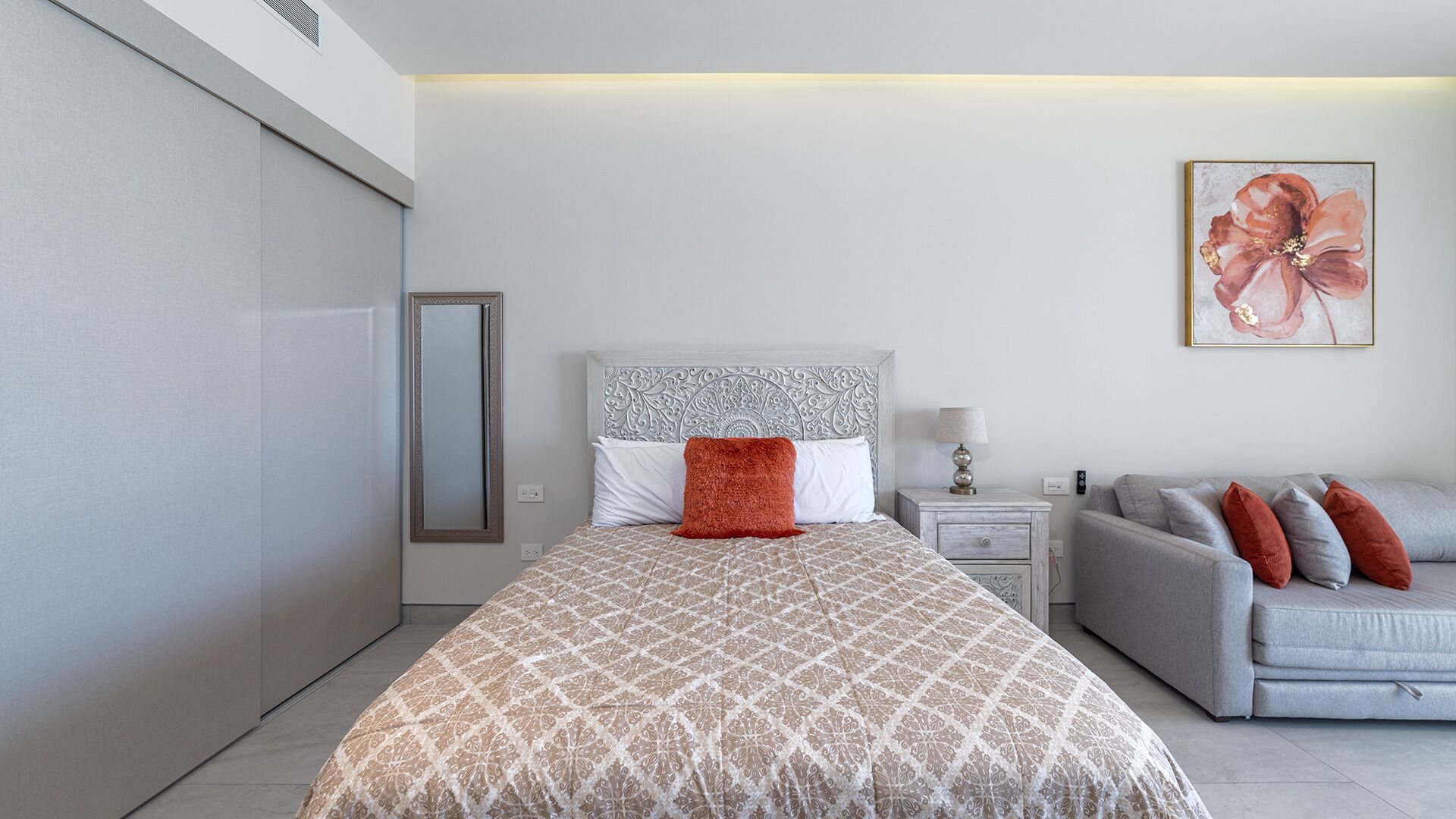 A modern bedroom with a patterned bedspread, a grey sofa, and a decorative wall piece.