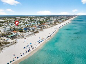An aerial view of a coastal town with a long sandy beach, clear turquoise waters, and a dense cluster of buildings along the shore. - My Destin Vacation - Gulf Views & Private Pool (Destin)