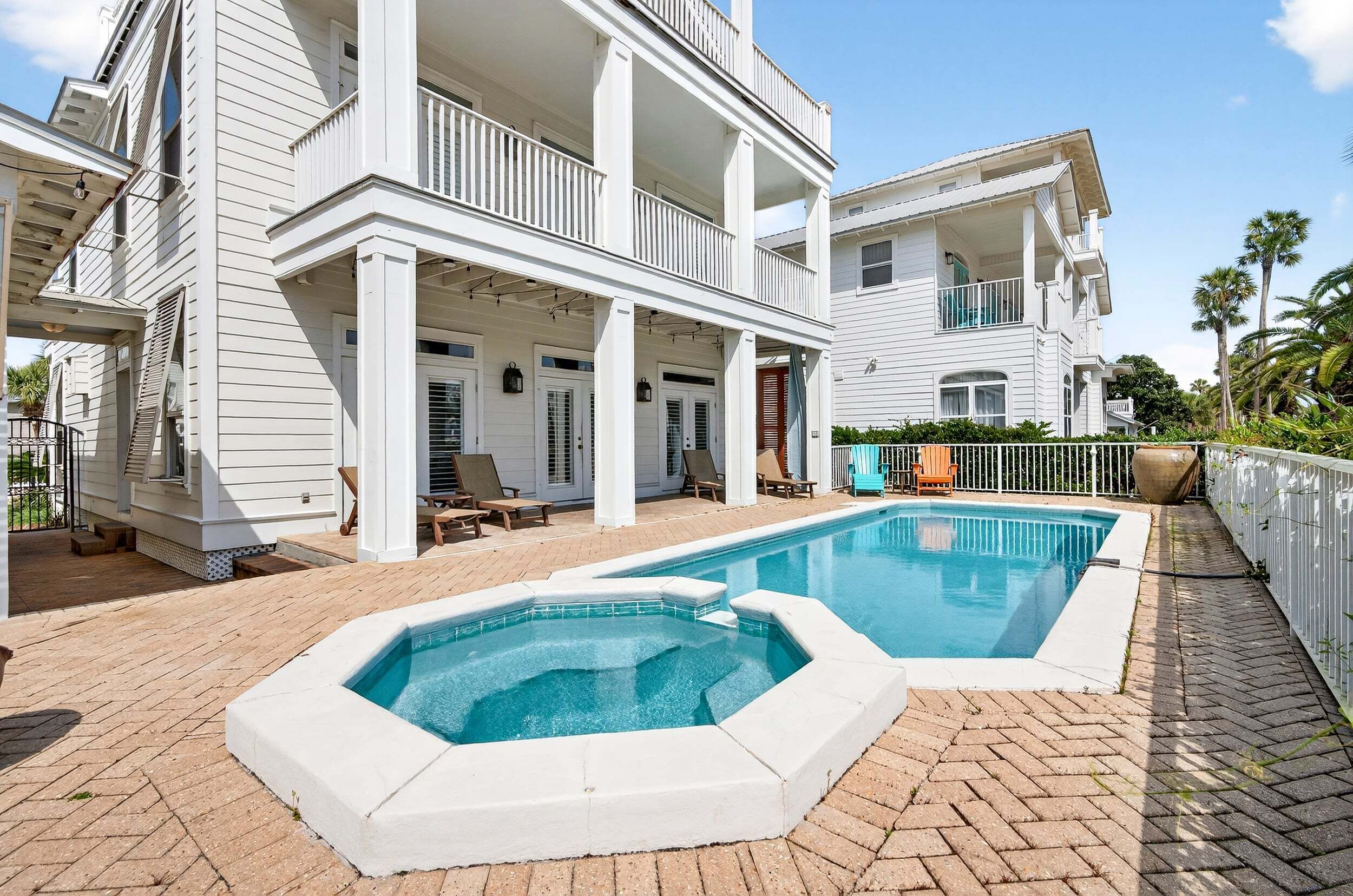 A two-story house with a swimming pool, outdoor seating, and a fenced patio area.