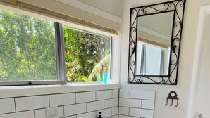 A compact kitchen with a washing machine, a sink, and a window with a view of greenery. - Mission Retreat - spacious and peaceful (Kerikeri)
