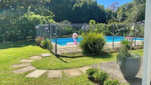 A swimming pool surrounded by a fence, with a pink flamingo decoration, and a garden with various plants and a large planter. - Mission Retreat - spacious and peaceful (Kerikeri)