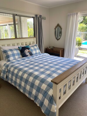 Ein Schlafzimmer mit kariertem Bettbezug, einem hölzernen Kopfteil, einem Nachttisch, einem Spiegel und Blick auf einen Swimmingpool.