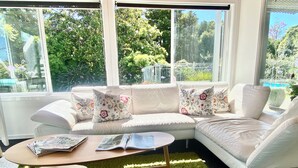 A modern living room with a sectional sofa, a coffee table, and a view of a garden through large windows. - Mission Retreat - spacious and peaceful (Kerikeri)