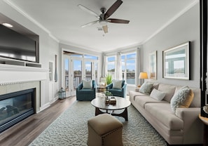 A living room with a fireplace, a ceiling fan, a large window, and a sofa.