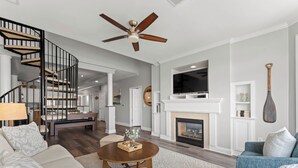 Un salon moderne avec une cheminée, un téléviseur, un ventilateur de plafond et un escalier.