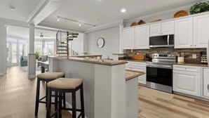 Une cuisine moderne avec des meubles blancs, un îlot central et un escalier menant à un autre niveau.