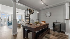 Un vaste espace de vie comprenant une table à manger en bois, un banc intégré, un escalier en colimaçon et une horloge au mur.