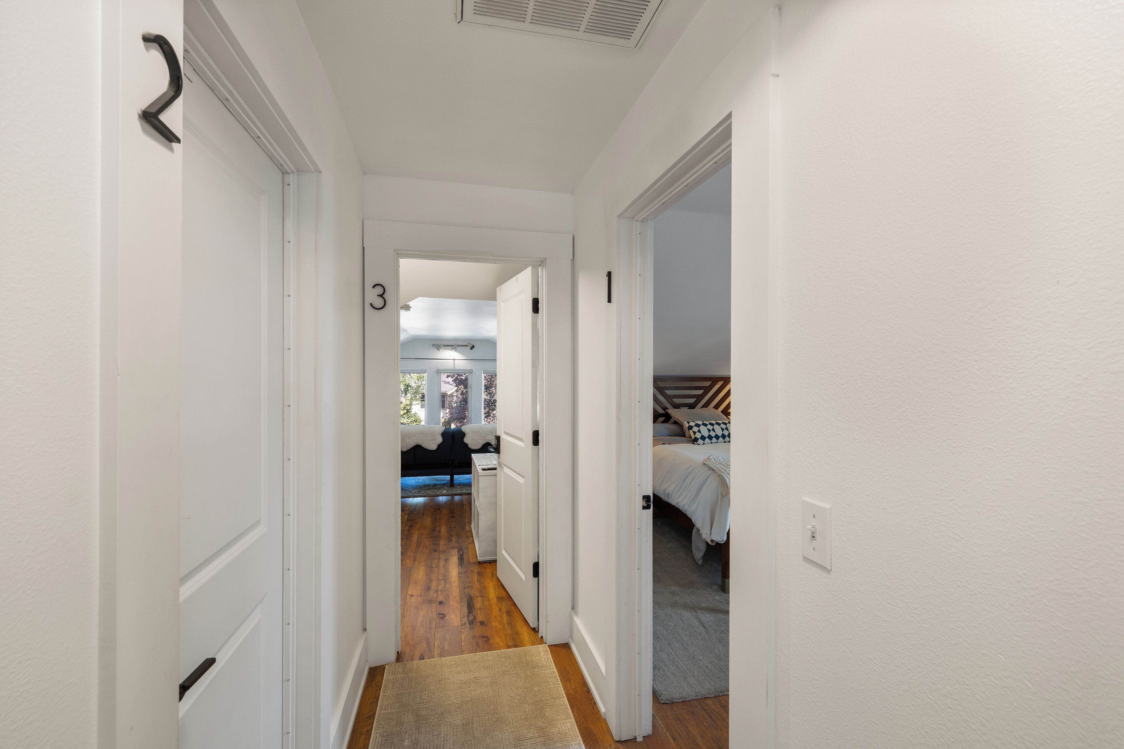 A narrow hallway with white walls, wooden flooring, and numbered doors leading to different rooms.