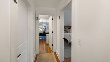 A narrow hallway with white walls, wooden flooring, and numbered doors leading to different rooms.