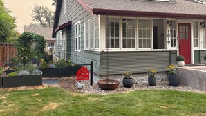 Una casa de dos pisos con puerta roja, ventanas de marco blanco y exterior gris.