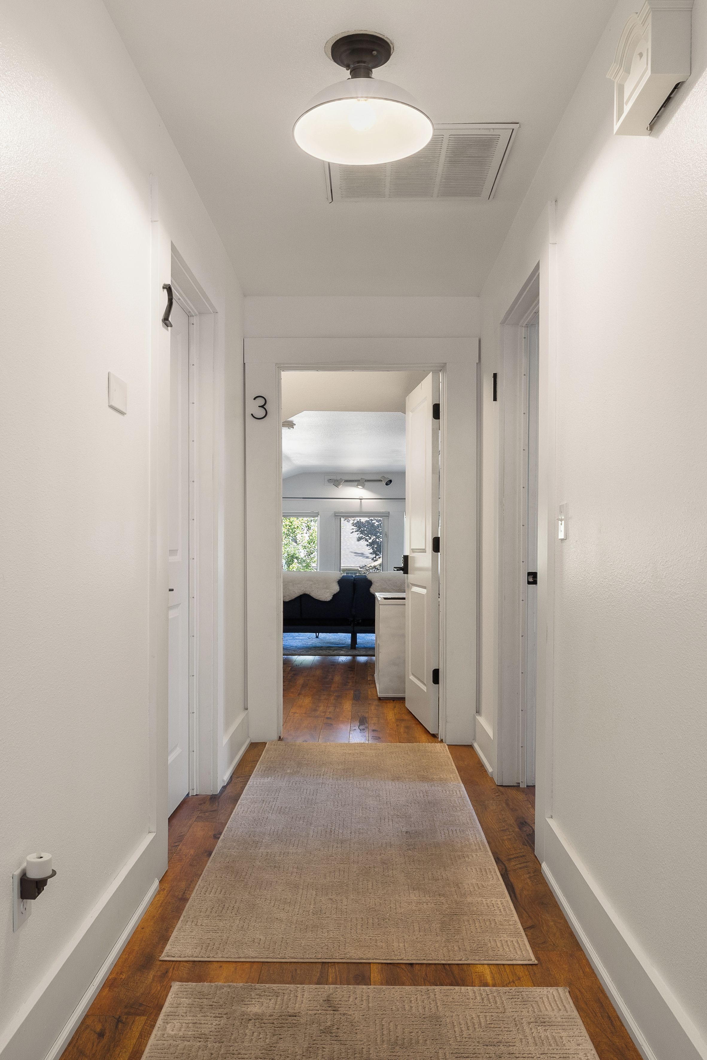A hallway with a wooden floor, white walls, and a ceiling light fixture.