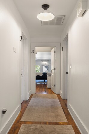 A hallway with a wooden floor, white walls, and a ceiling light fixture.