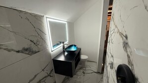 Et badeværelse med marmorgulv, en sort vask, et hvidt toilet og et spejl med lys.
