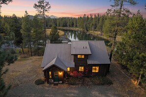 A log cabin with a metal roof, surrounded by a forest and a lake. - Sunriver Riverfront Log Cabin With Hot Tub (Bend)