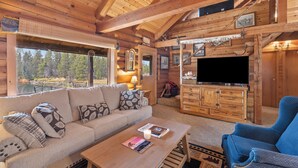 Interior d'una cabana de fusta amb un sofà, una televisió i una llar de foc.