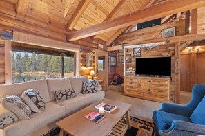 A log cabin interior with a sofa, a television, and a fireplace. - Sunriver Riverfront Log Cabin With Hot Tub (Bend)
