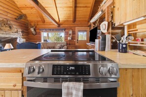 A kitchen with a stainless steel stove, wooden cabinets, and a view of the living area. - Sunriver Riverfront Log Cabin With Hot Tub (Bend)