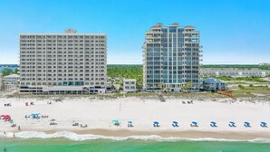 Ein Strandhotel mit mehreren Etagen, einem Sandstrand und einem klaren, blauen Himmel.
