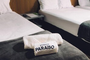 Ett hotellrum med två sängar, ett nattduksbord och en hopvikt handduk med texten ”ESPAÇO PARAÍSO”.