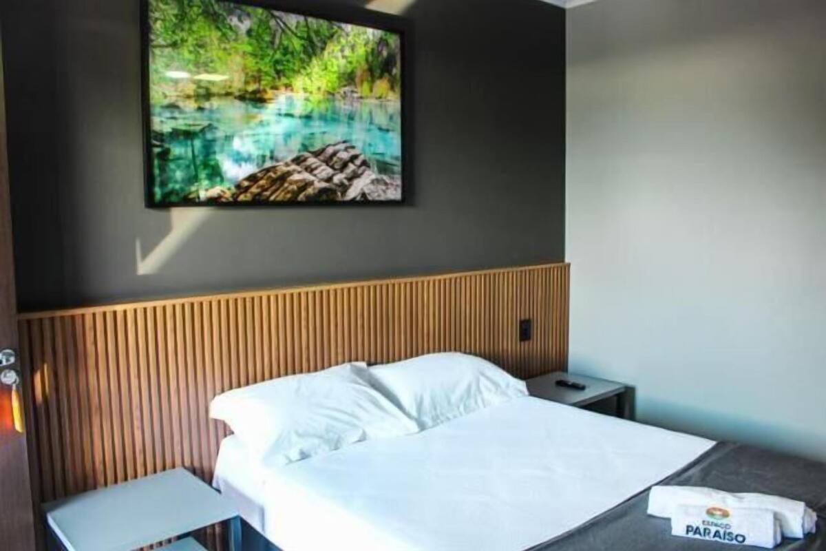 A hotel room with a bed, a nightstand, a wall-mounted TV, and a wooden headboard.