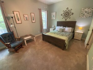 A bedroom with a bed, a chair, a nightstand, a lamp, and framed pictures on the wall. - Piece of Peace, Full Home, Quiet, Private, Yet Close to Everything, 3 bed/2 bath (Abita Springs)