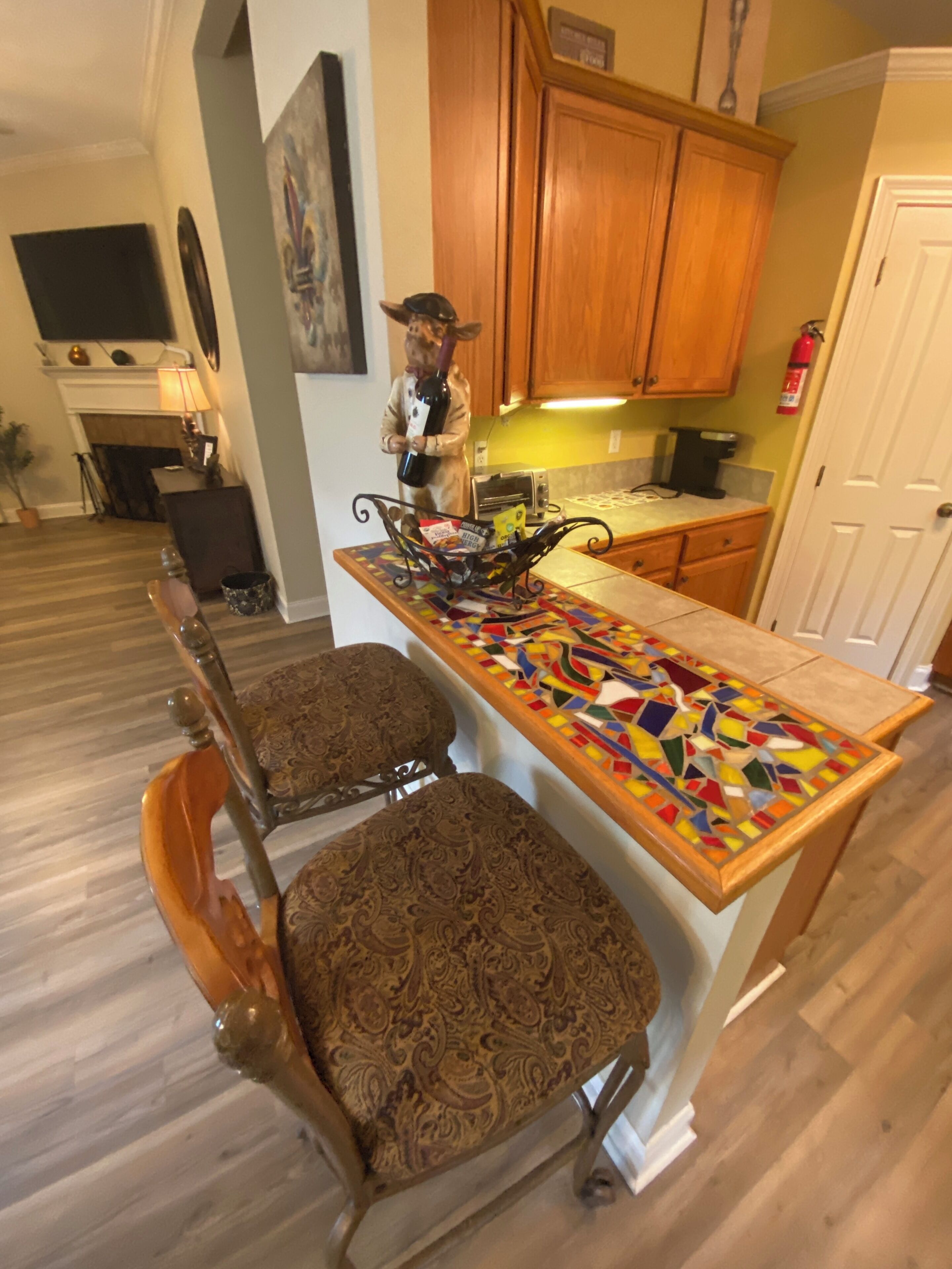 Une cuisine avec des meubles de rangement en bois, un pare-feu en carreaux et une statue décorative. On y trouve deux fauteuils rembourrés aux motifs complexes.