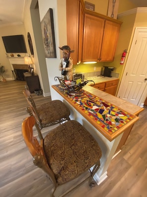 Una cocina con armarios de madera, salpicadero de azulejos y una estatua decorativa. Hay dos sillas tapizadas con diseños elaborados.
