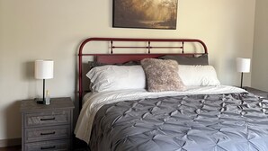 Ein Schlafzimmer mit einem Bett, Nachttischen, einer Lampe, einem Bild an der Wand und einem gemusterten Teppich.
