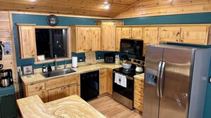 A kitchen with wooden cabinets, a stainless steel refrigerator, a microwave, and a dishwasher. - Greer Mountain Cabin: Scenic Deck, Rustic Charm & Stress-Free Parking (Greer)